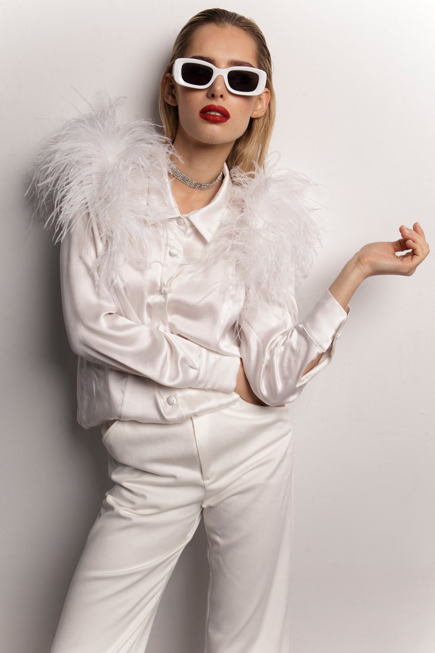 Koszula Heron w ujęciu portretowym – modelka w białych okularach przeciwsłonecznych eksponuje pióra na ramionach. Jedwabna tkanina subtelnie połyskuje, a geometryczny kołnierz dodaje koszuli nowoczesności. To odważny element garderoby, idealny dla osób pragnących wyróżnić się niebanalnym dodatkiem – koszula z piórami Heron to synonim luksusu i kreatywnej elegancji.