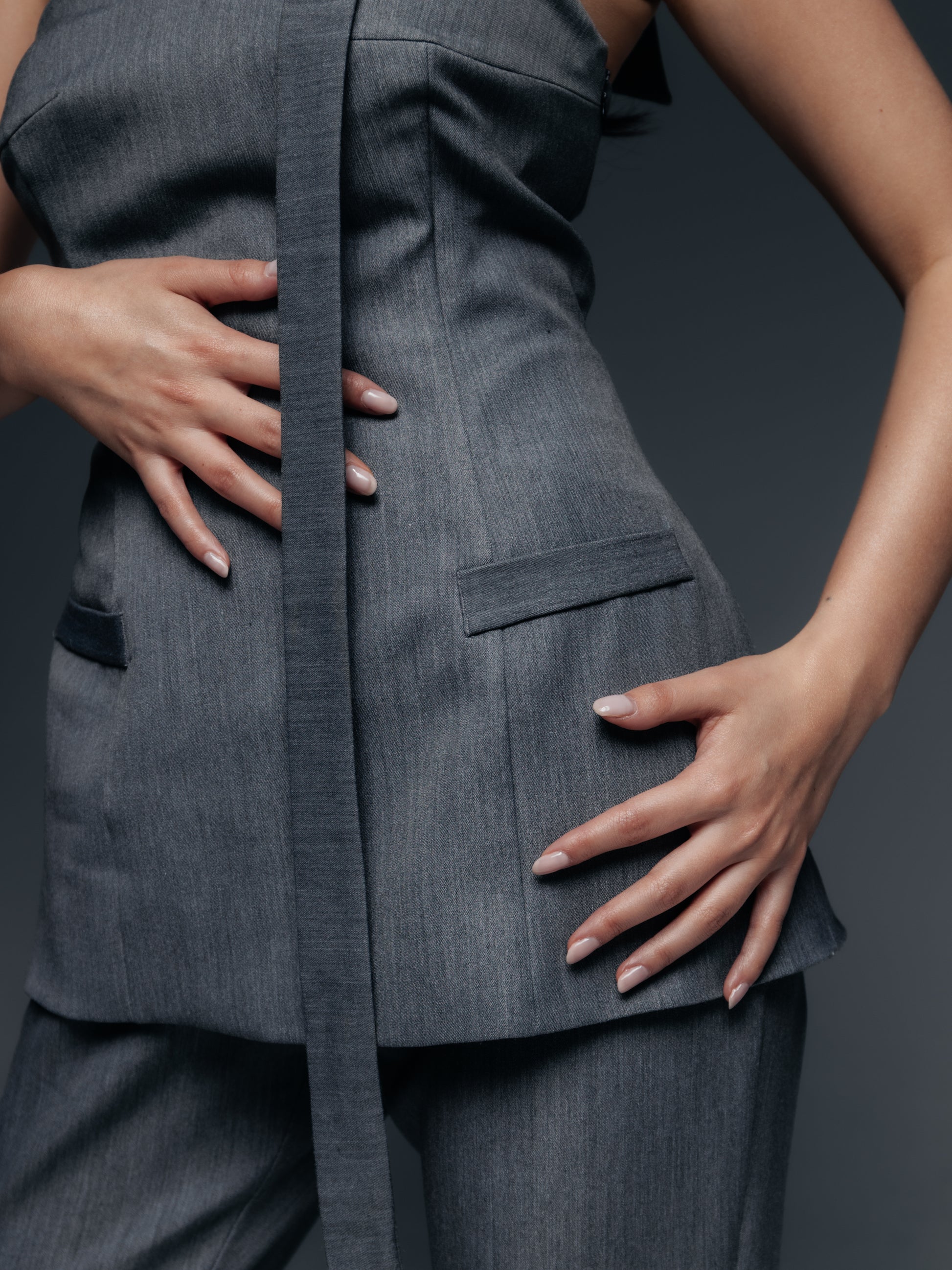 Detal gorsetu Mars w okolicy talii. Pionowe cięcia i wszyte fiszbiny modelują figurę, podkreślając wcięcie w talii. Materiał o delikatnym, garniturowym prążkowaniu układa się gładko, a elastyczność tkaniny pozwala na komfortowy ruch.  Z przodu, na środku, można dostrzec subtelne zapięcie –  wszystko utrzymane w tej samej szarości, co czyni projekt spójnym. Ten zbliżony kadr pokazuje kunszt krawiecki topu Mars: precyzyjne szycia, wzmacniające fiszbiny i przemyślane detale sprawiają, że gorset leży idealnie.