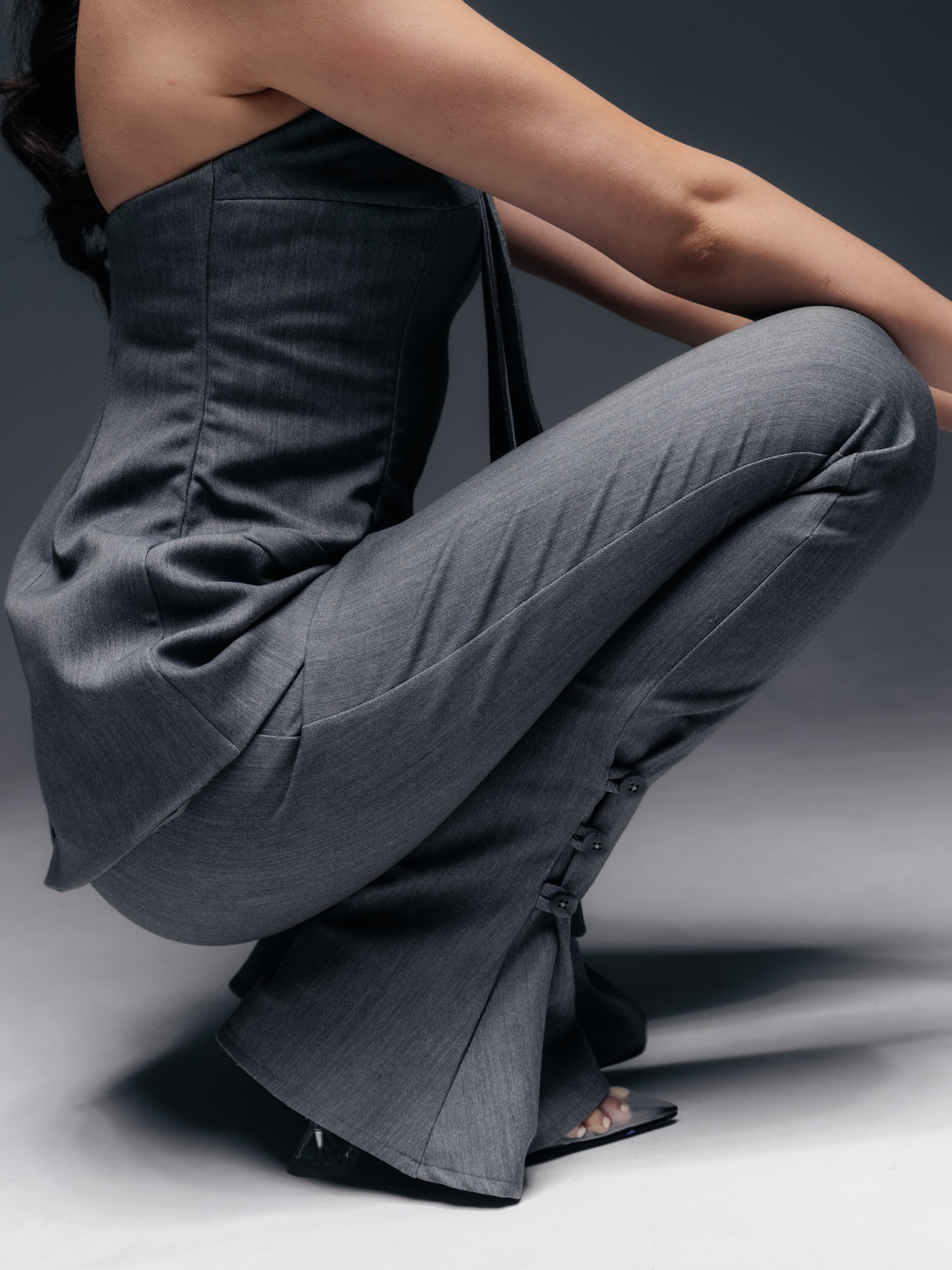 Zbliżenie na dolną część spodni Mars – widoczny jest klin (godet) rozszerzający nogawkę przy kostce oraz trzy funkcjonalne guziki, które można rozpiąć dla uzyskania efektu rozcięcia. Szara tkanina o delikatnym prążku układa się gładko na nodze, a precyzyjne cięcia krawieckie podkreślają wysoką jakość wykonania. Ten detal sprawia, że klasyczne garniturowe spodnie nabierają wyjątkowego charakteru i lekkości ruchu, będąc jednocześnie praktyczne i stylowe.
