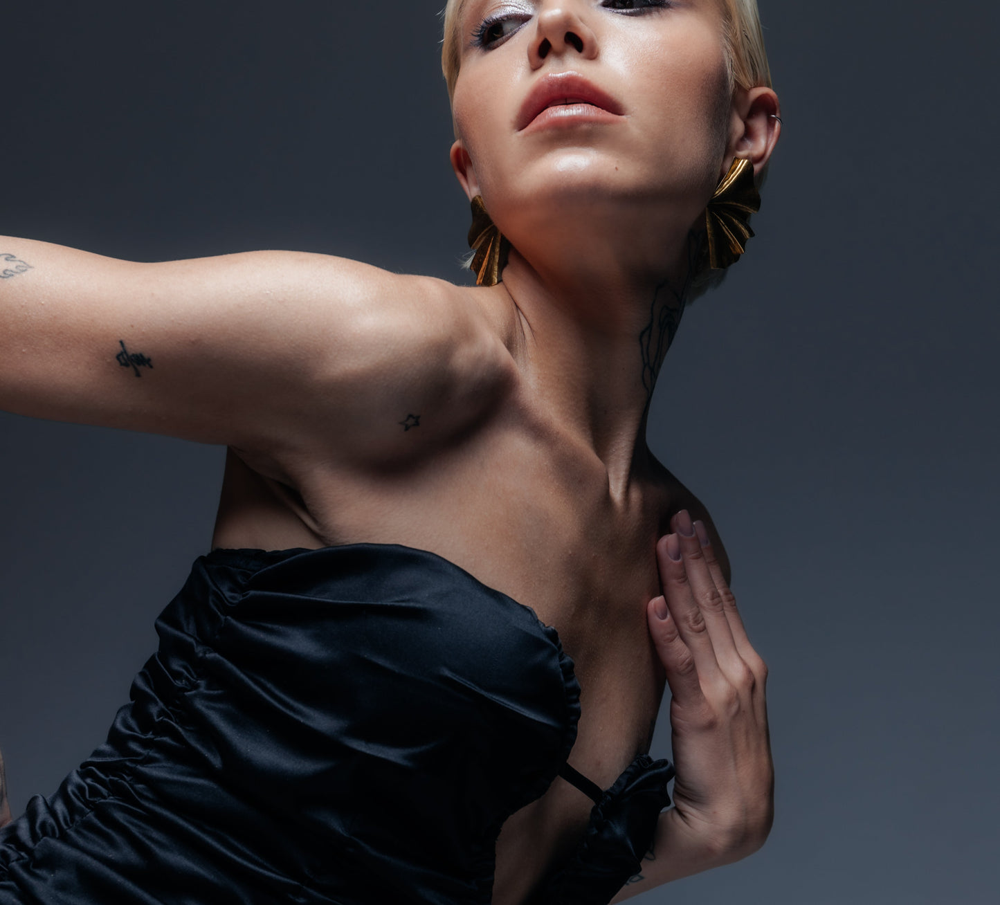 Widać szczegółowo sercowaty kształt gorsetu oraz wycięcie na środku, przewiązane cienką czarną tasiemką, która tworzy ozdobną pętelkę wzmacniającą brzegi dekoltu. Satynowa tkanina pięknie odbija światło, ukazując głębię czerni i strukturę marszczeń. To sensualny detal, który przyciąga spojrzenia ku dekoltowi, pozostając jednocześnie w granicach elegancji – sukienka uwodzi formą, a nie nadmiernym odsłonięciem.