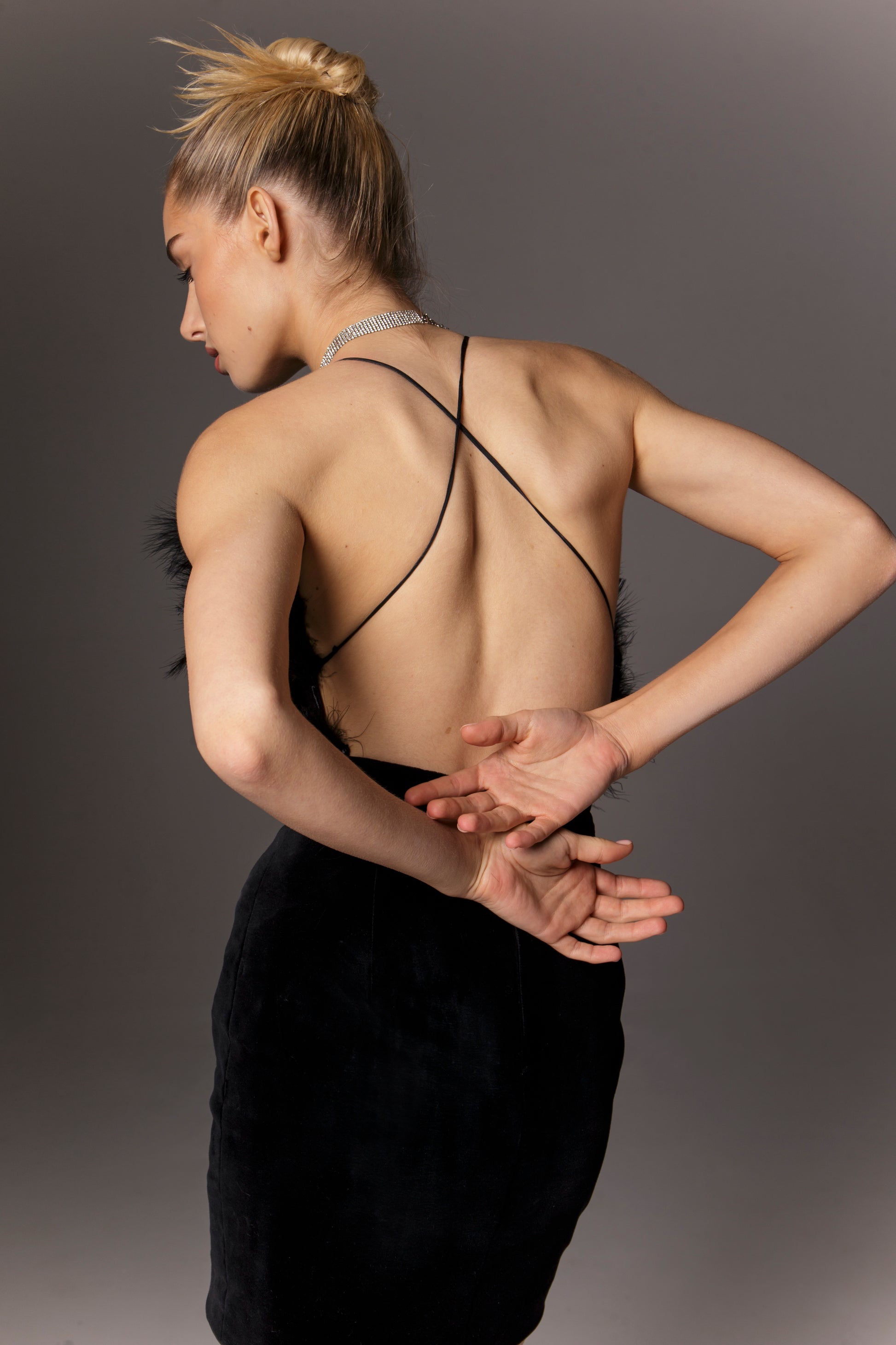 Tylny widok sukienki Blackbird przedstawia odkryte plecy z krzyżującymi się cienkimi ramiączkami. Czarna aksamitna tkanina gładko przylega do ciała na wysokości talii i bioder, podkreślając figurę, podczas gdy plecy pozostają kusząco odsłonięte. Krzyżujące się ramiączka dodają stabilności konstrukcji gorsetu i jednocześnie stanowią dekoracyjny element. Ujęcie to ukazuje, jak sukienka łączy w sobie elegancję i śmiałość – mieniący się aksamit i pióra z przodu, kontrastujące z prostym, seksownym tyłem.